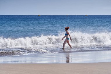 Güneşli bir günde Playa de la Tejita 'da mayo giymiş bir kadın dalgaların arasında yürüyor.