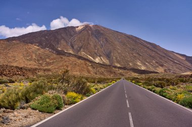 Tenerife 'de berrak mavi bir gökyüzünün altındaki Teide volkanının dik kayalık yamaçlarına doğru düz bir yol.