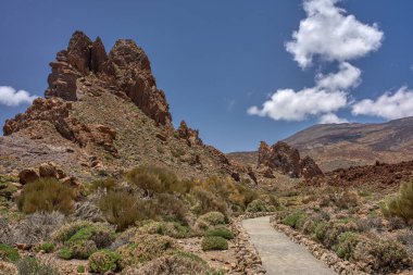 Volkanik yürüyüş yolu Roques de Garcia yakınlarındaki kayalık arazide Pico del Teide ile birlikte mavi bir gökyüzünün altında dönüyor.