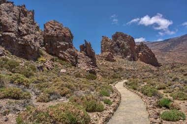 Kurak volkanik arazide, güneşli bir gökyüzünün altında, Roques de Garcia 'nın kaya oluşumlarına doğru giden kıvrımlı yürüyüş yolu.