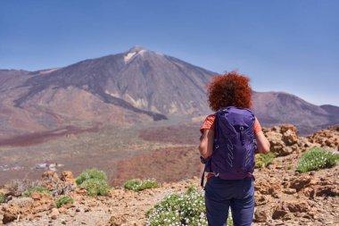 Uçsuz bucaksız volkanik manzaraya ve Teide Ulusal Parkı 'ndaki Pico del Teide' e bakan kayalık yolda duran kadın yürüyüşçü.