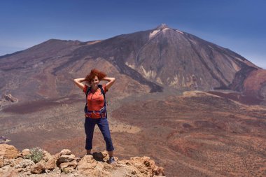 Tenerife 'de güneşli bir günde Pico del Teide' nin önünde güvenle poz veren kızıl saçlı kadın yürüyüşçü.