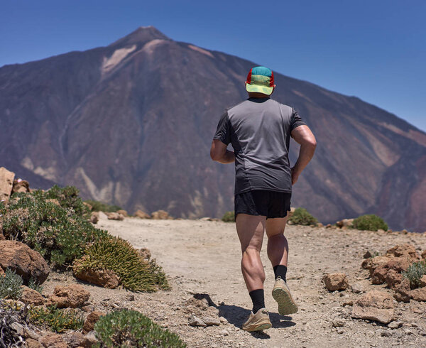 Тропа бегун восхождения на гору Гуахара с Пико дель Тейде растет на заднем плане на солнечном вулканическом склоне