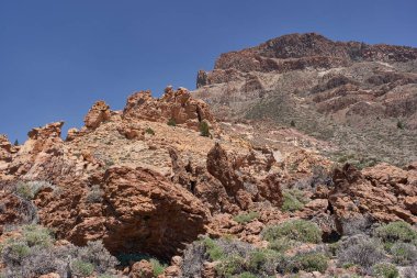 Arkaplanda yükselen Guajara Dağı ile berrak mavi gökyüzünün altında volkanik kayalık yamaç