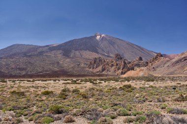 Llano de Ucanca ovası seyrek volkanik bitki örtüsüyle, Roques de Garcia ve Pico del Teide açık bir gökyüzünün altında