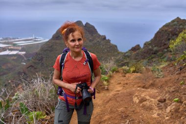 Arka planda Punta del Hidalgo kıyı kasabası olan dik Chinamada patikasında yürüyüş yapan bir kadın.