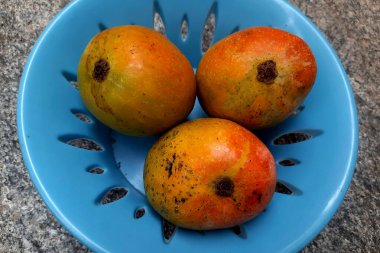 Mavinin içine yerleştirilmiş kırmızı, olgun mango meyvelerinin daha yakın görüntüsü, plastik tepsi