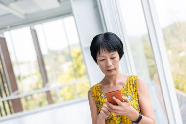 olgun Asyalı kadın modern bir binada cep telefonu kullanarak