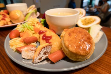 Sosis, kızarmış balık, sebze, çörek ve yemek takımının bulanık arka planına sahip bir fincan çorba da dahil olmak üzere çeşitli kahvaltı malzemeleri..