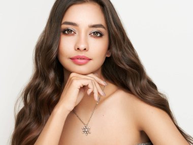 Beyaz arka planda poz veren kokteyl elbiseli güzel bir kadın. Uzun kıvırcık saçlı güzellik mankeni. Noel ya da yeni yıl şenlikleri. Mücevher ve manikür.