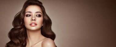 Mükemmel makyajlı esmer kız. Uzun kıvırcık saçlı, gülümseyen güzel model kadın. Bakım ve güzellik saç ürünleri
