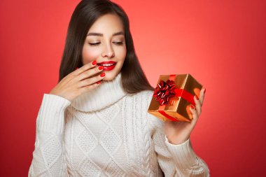 Kırmızı arka planda izole edilmiş hediye kutusuyla beyaz örülü süveter içinde çok güzel. Noel ya da yeni yıl şenlikleri. Tatil ve Parti