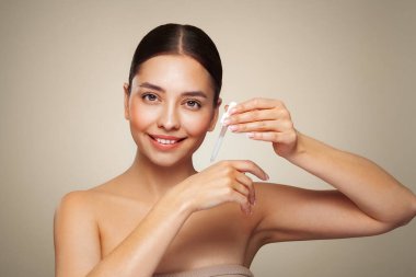 Genç ve güzel bir kadın pipetle yüz serumu uyguluyor. Yüz bakımı için estetik prosedürler