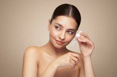 Genç ve güzel bir kadın pipetle yüz serumu uyguluyor. Yüz bakımı için estetik prosedürler