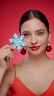 Kurabiyeden yapılmış kar tanesiyle güzel bir genç kadın, kırmızı arka planda izole edilmiş. Noel ya da yeni yıl şenlikleri. Tatil ve Parti. Yavaş çekim dikey video