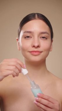 Yüzünde pipetle yüz serumu uygulayan genç ve güzel bir kadın. Yüz bakımı için estetik prosedürler. Yavaş çekim, dikey video