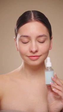 Elinde kozmetik yağ serumu ya da hyaluronik asit dolu bir kavanoz tutan güzel genç kadın. Mükemmel bir yüz derisi. Kozmetik cilt bakımı. Yavaş çekim, dikey video