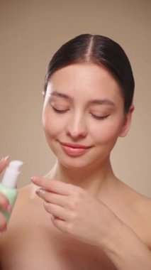 Genç bir kadının portresi, yüzünün kremlerini kullanıyor. Taze nemlendirilmiş cilt, güzel yakın plan kozmetik yüz, mutlu sağlıklı model. Yüz kremi şişesi olan bir model. Yavaş çekim, dikey video