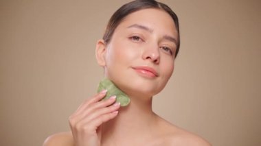 Cilt bakımı rutini yapan güzel genç bir kadın, hurda, yüz masajı, yeşim taşıyla yüz bakımı, yaşlanma ve kozmetik temizleme için yüz bakımı. Yavaş çekim