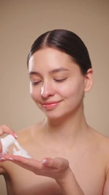 Genç bir kadın yüzünü köpükle yıkar. Günlük yüz bakımı rutini. Yakından görüntü, yavaş çekim 4K görüntü, dikey video