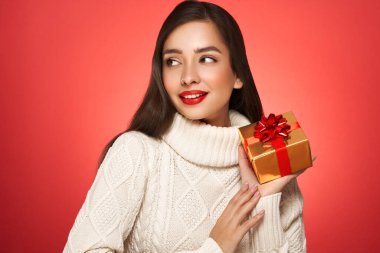 Kırmızı arka planda izole edilmiş hediye kutusuyla beyaz örülü süveter içinde çok güzel. Noel ya da yeni yıl şenlikleri. Tatil ve Parti