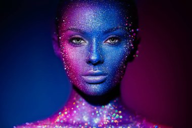Mavi parlak parıltılı ve neon ışıklı model kadın stüdyoda poz veriyor. Güzel genç bir kadının portresi. Sanat tasarımı rengarenk parıltılı makyaj