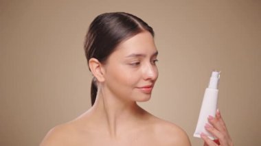 Bir şişe nemlendirici kremi olan güzel bir kadın. Bej arka planda mükemmel cilde sahip bir kadının videosu. Güzellik ve Deri Bakımı konsepti. Yavaş çekim