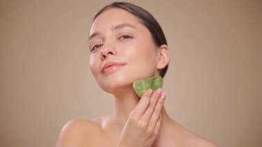 Cilt bakımı rutini yapan güzel genç bir kadın, hurda, yüz masajı, yeşim taşıyla yüz bakımı, yaşlanma ve kozmetik temizleme için yüz bakımı. Yavaş çekim