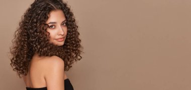 Saçları kıvırcık, gülümseyen güzel bir kadının moda stüdyo portresi. Moda ve güzellik