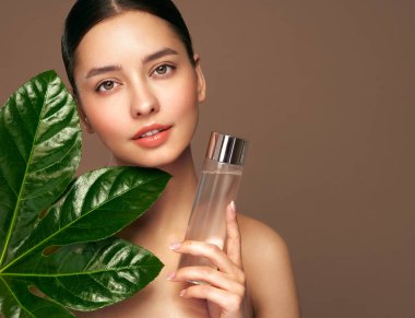 Yeşil egzotik yapraklı kadın yüzünü kapat. Cilt bakımı güzellik tedavisi konsepti. Yüzü temiz ve sağlıklı bir model. Kadın şişeyi kozmetik tonikle tutuyor.