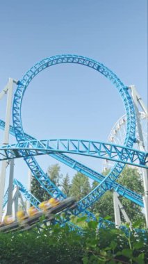 Mavi gökyüzüne karşı lunapark treni. Lunaparktaki lunaparkta hız treni. Eğlence parkında keyifli eğlenceler. Dikey video