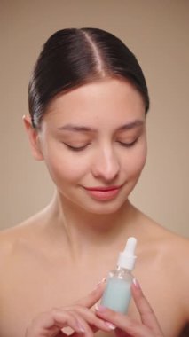 Elinde kozmetik yağ serumu ya da hyaluronik asit dolu bir kavanoz tutan güzel genç kadın. Mükemmel bir yüz derisi. Kozmetik cilt bakımı. Yavaş çekim, dikey video