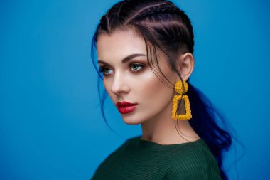 Mükemmel makyajlı esmer kız. Kıvırcık saçlı güzel bir model kadın. Bakım ve güzellik ürünleri. Saçları örgülü bir kadın. Mücevherleri olan bir model. Mavi arkaplan