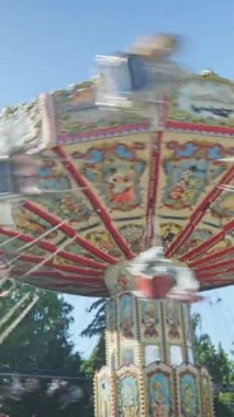 Güneşli bir günde insanlar atlıkarıncaya binerken eğlenirler. Eğlence parkında keyifli eğlenceler. Dikey yavaş çekim videosu