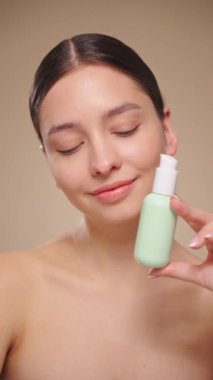 Genç bir kadının portresi, yüzünün kremlerini kullanıyor. Taze nemlendirilmiş cilt, güzel yakın plan kozmetik yüz, mutlu sağlıklı model. Yüz kremi şişesi olan bir model. Yavaş çekim, dikey video