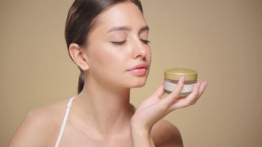 Genç bir kadının portresi, yüzünün kremlerini kullanıyor. Taze nemlendirilmiş cilt, güzel yakın plan kozmetik yüz, mutlu sağlıklı model. Yüz kremi kavanozu olan bir model.