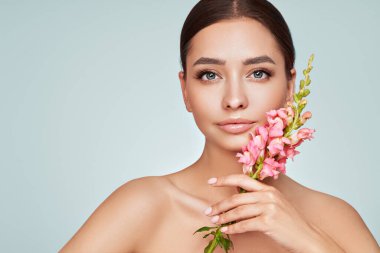 Temiz tenli güzel bir genç kadın portresi. Sağlıklı ciltli bir model, yakın portre. Kozmetik, güzellik ve kaplıca. Pembe çiçekli kız