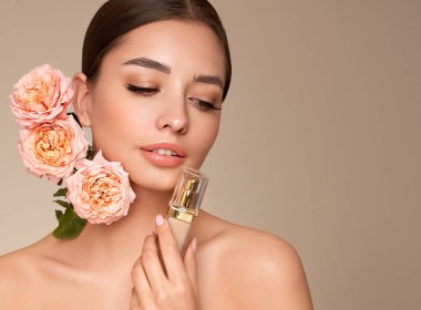 Temiz tenli güzel bir genç kadın portresi. Makyaj şişesi olan bir model. Gül çiçekli güzel bir kadın.