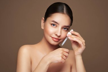 Genç ve güzel bir kadın pipetle yüz serumu uyguluyor. Yüz bakımı için estetik prosedürler