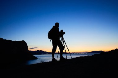 Gün batımında dağın tepesindeki fotoğrafçının silueti. Doğa fotoğrafçısı iş başında. Film analog fotoğrafçılık