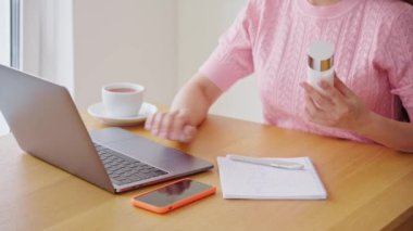 Ev mutfağında dizüstü bilgisayarla çalışan genç bir kadın. Evde çalış. Serbest, uzaktan kumandalı. Kadınlar internette kozmetik ürünleri reklamları yapıyor.