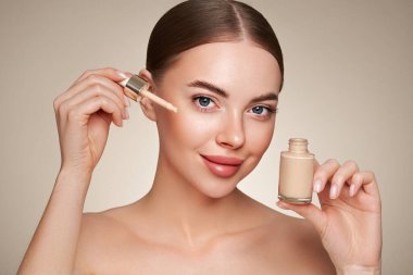 Temiz tenli güzel bir genç kadın portresi. Makyaj şişesi olan bir model. Kozmetik, güzellik ve kaplıca