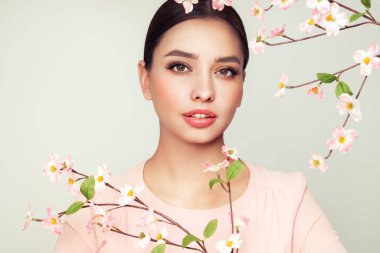 Kiraz çiçeği dallı güzel bir genç kadın. Temiz ciltli bir model, yakın portre. Kozmetik, yüz bakımı, güzellik ve kaplıca