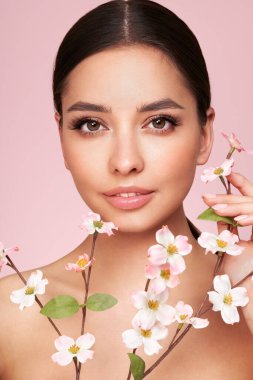 Kiraz çiçeği dallı güzel bir genç kadın. Temiz ciltli bir model, yakın portre. Kozmetik, yüz bakımı, güzellik ve kaplıca