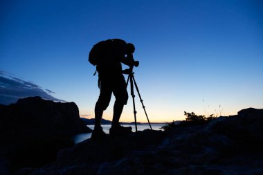 Gün batımında dağın tepesindeki fotoğrafçının silueti. Doğa fotoğrafçısı iş başında. Film analog fotoğrafçılık
