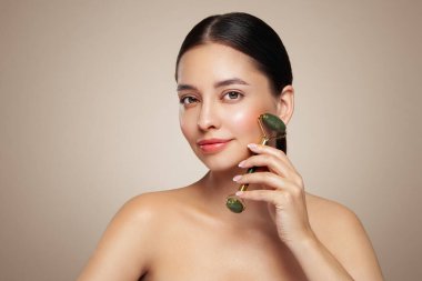 Doğal bir yeşim taşlı rulo kullanırken rahat ve gülümseyen genç bir kadının videosunu kapat. Deri silindirli yaşlanma ve kozmetik temizliği için yüz bakımı.