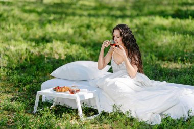 Kadın bir yaz ormanında uyanıyor. Genç bir kadın yaz ormanında yatakta kahvaltı yapıyor.