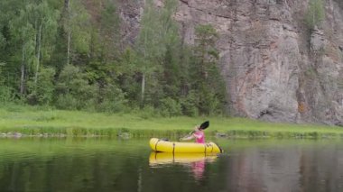 Kadın gezgin dağ nehrinde yüksek dağlarla çevrili bir teknede yüzüyor. Kız kano raftingi sakin nehir boyunca kürek çekiyor. Paketleme