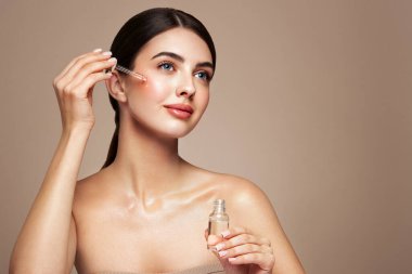 Genç ve güzel bir kadın pipetle yüz serumu uyguluyor. Yüz bakımı için estetik prosedürler