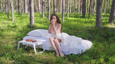 Kadın bir yaz ormanında uyanıyor. Bir kız sabah çayı içiyor ormandaki bir yatakta oturuyor.